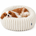 A brown and white dog lying inside a round, cream-colored ribbed pet bed on a white background.